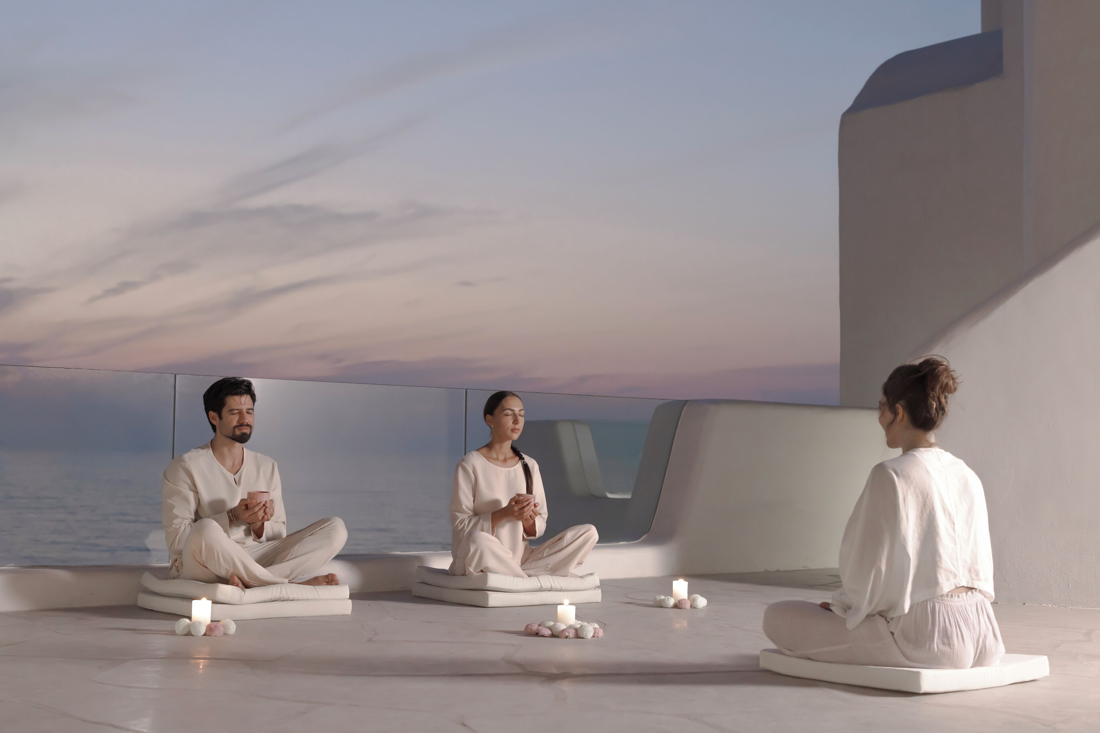 Three individuals meditating in a modern, minimalist room with a view of the sea.