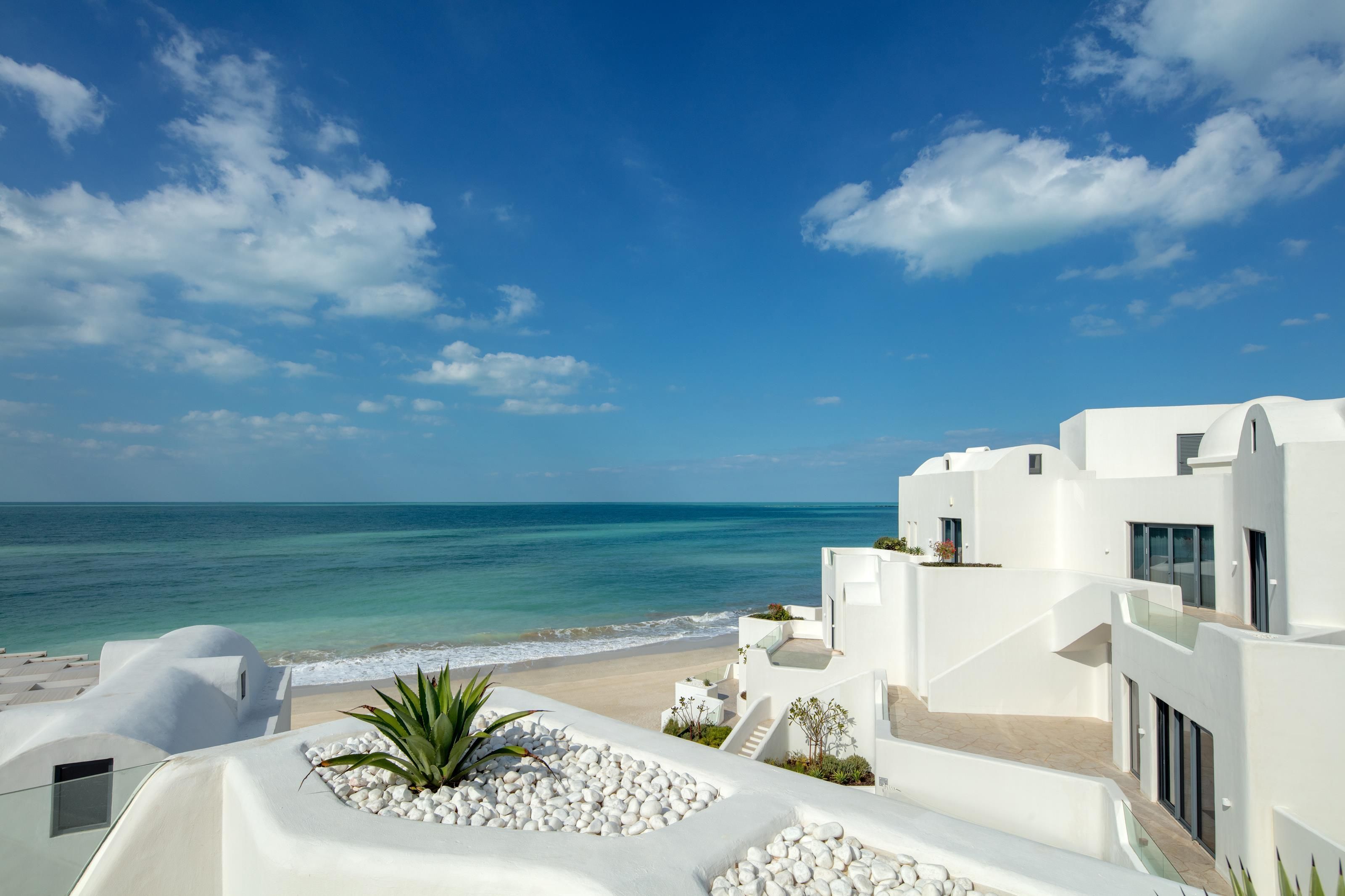 A coastal hotel with white architecture, a beach view, and a clear sky.