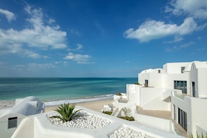 Un hôtel en bord de mer, doté d’une architecture blanche, offrant une vue sur la plage et s’ouvrant sur un ciel dégagé.