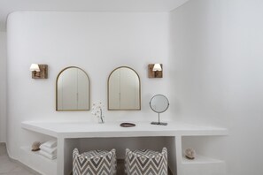 Un baño moderno con dos espejos grandes, un espejo redondo y un tocador con estantes.
