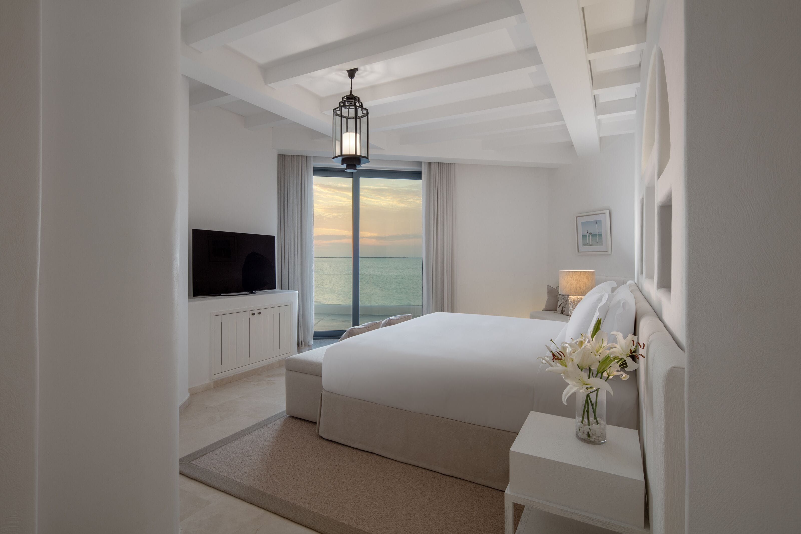 Une chambre d’hôtel moderne dotée d’un grand lit, d’une télévision, d’une table de chevet avec une lampe et offrant une vue sur la mer.