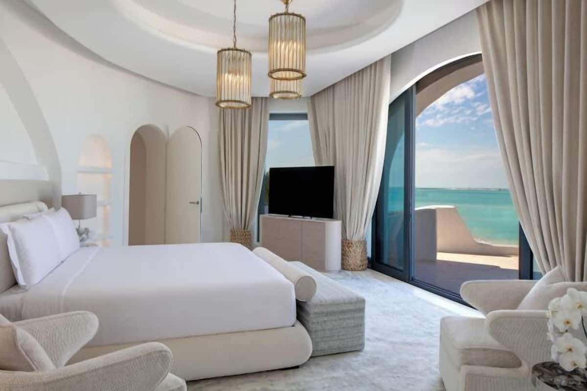 Una habitación de hotel moderna con una cama grande, un televisor y un balcón con vistas al océano.