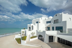 Un edificio moderno y blanco con vista al mar, que cuenta con una escalera que lleva a un balcón con barandilla de vidrio.