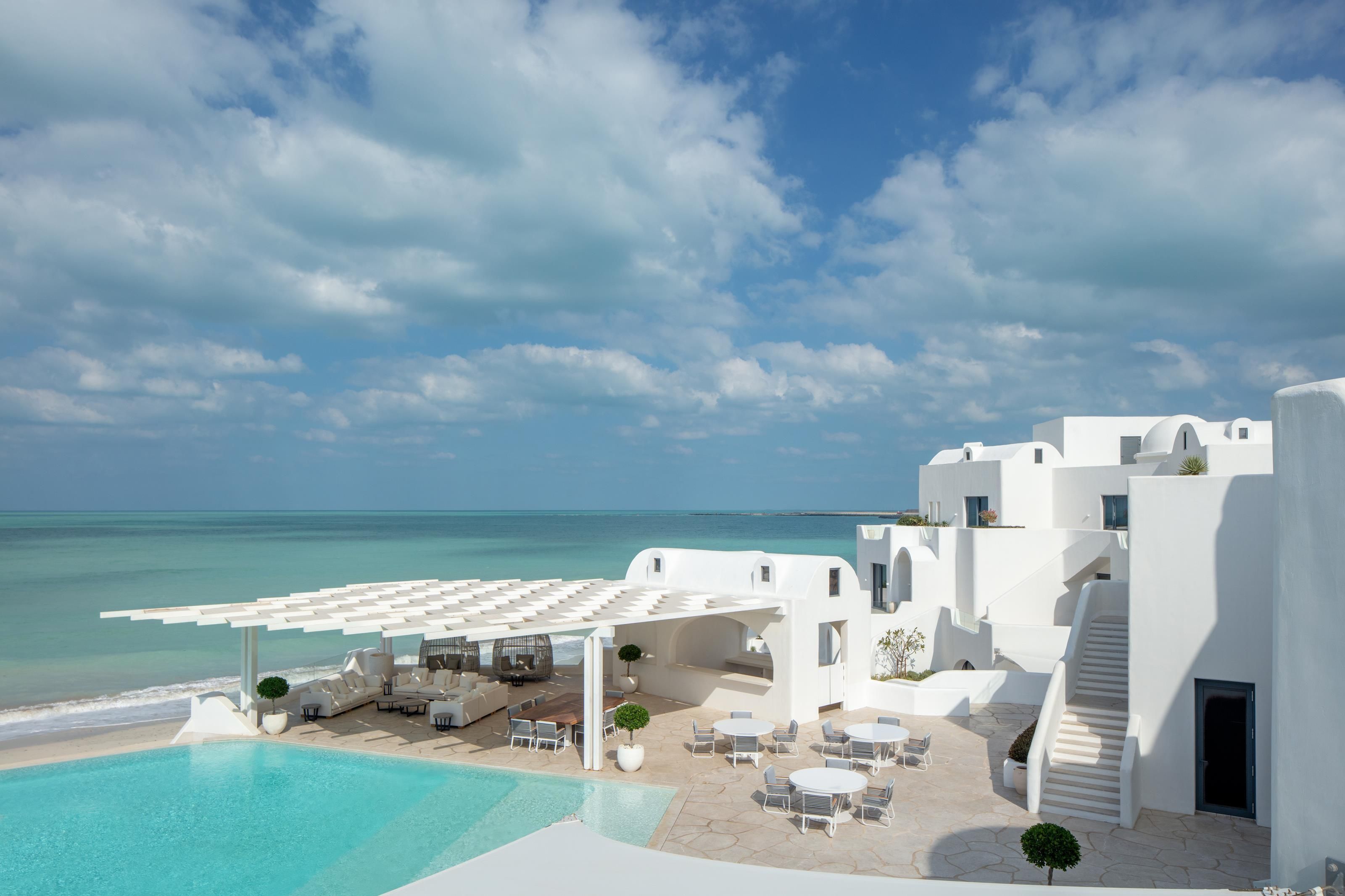 A resort with a pool, outdoor seating, and a view of the sea.