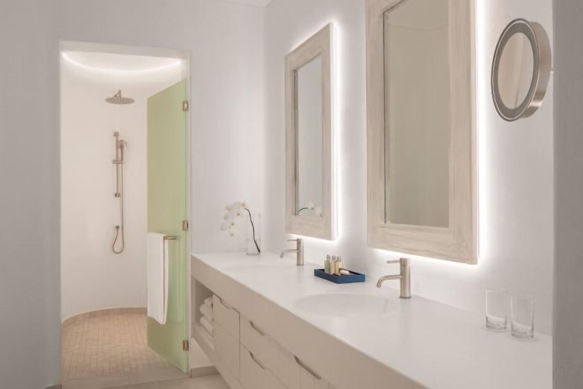 Une salle de bain moderne avec un meuble-lavabo blanc, un grand miroir et un espace douche.