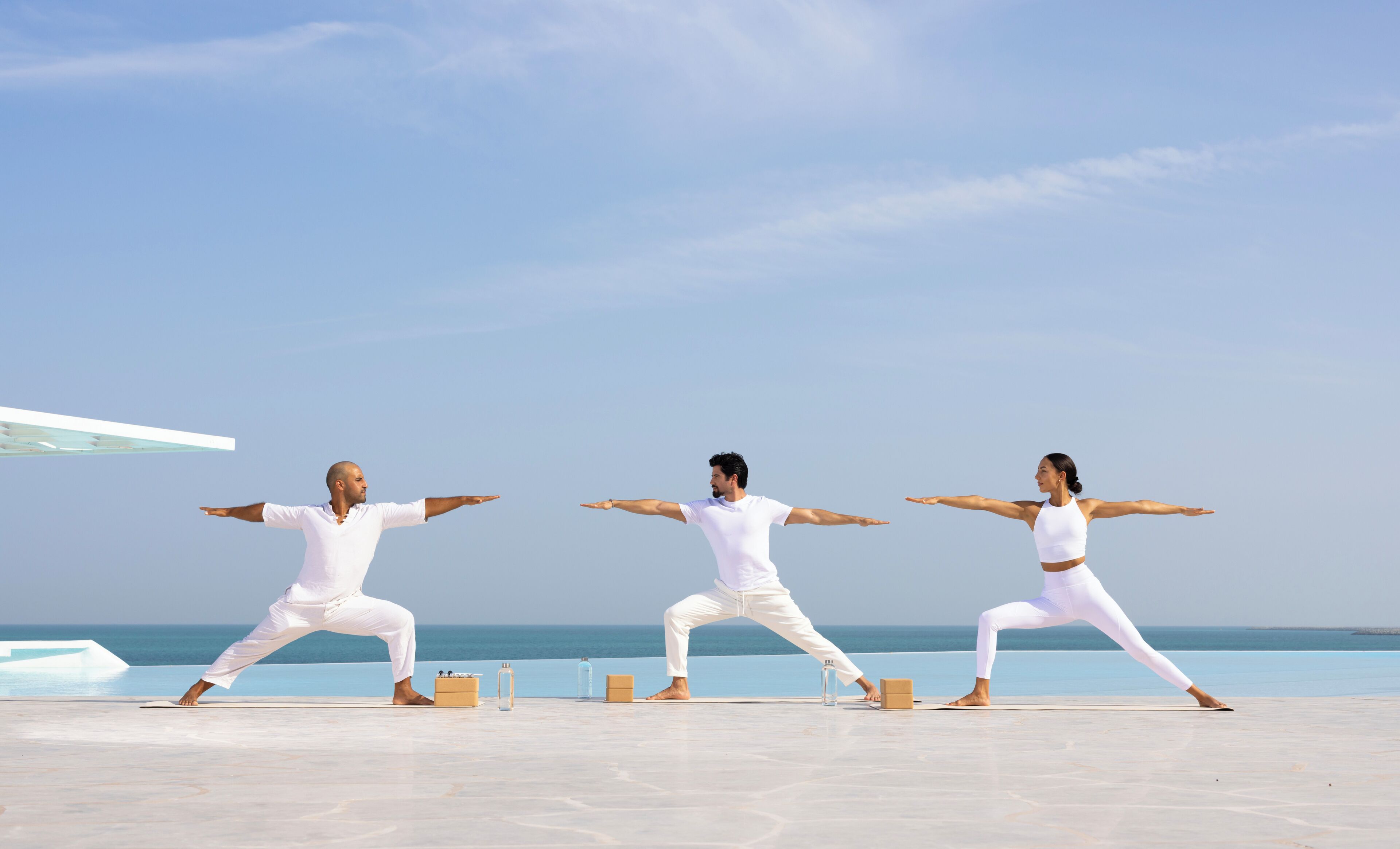 Drei Personen üben Yoga am Strand, im Hintergrund das Meer.