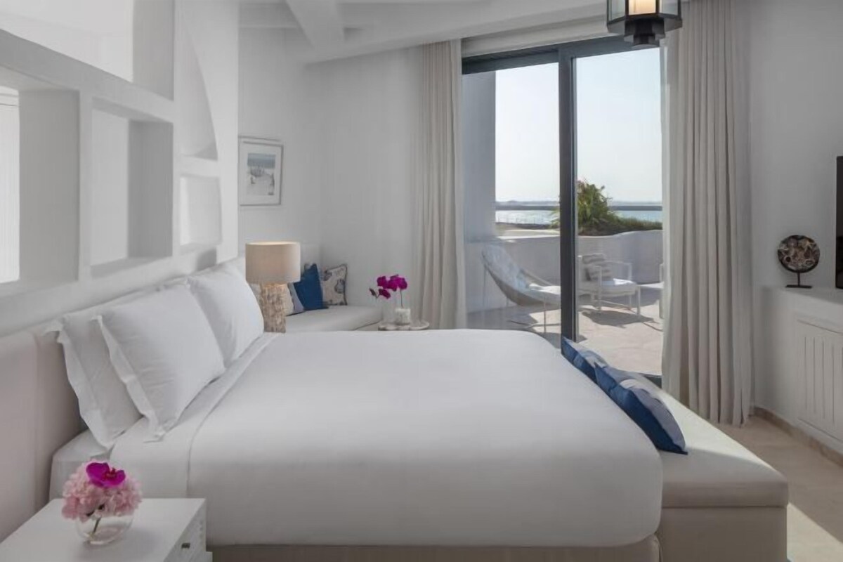 Ein modernes Hotelzimmer mit einem großen Bett, einem Balkon mit Blick und einer minimalistischen Einrichtung.