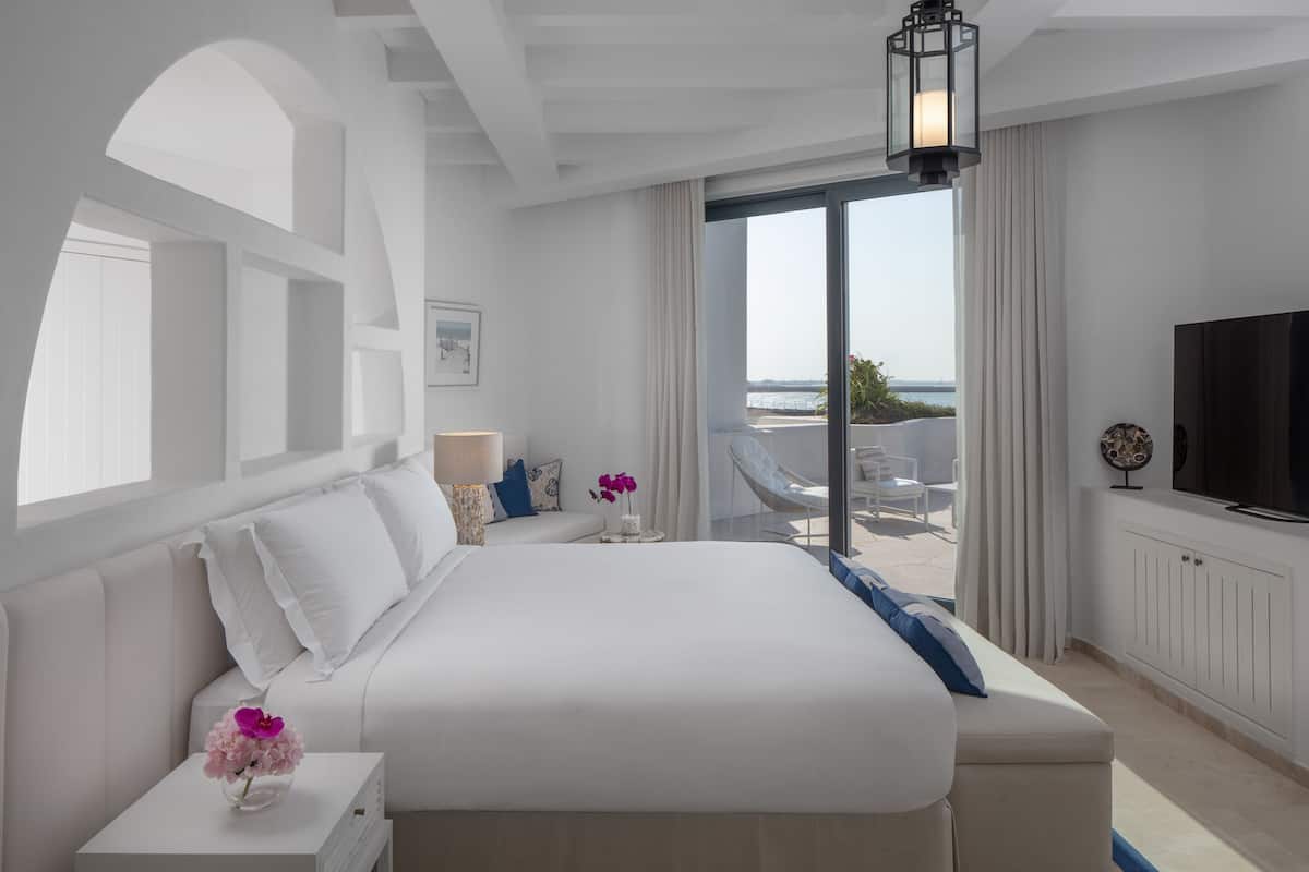 Una habitación de hotel moderna con una cama grande, un televisor y un balcón con vistas al mar.