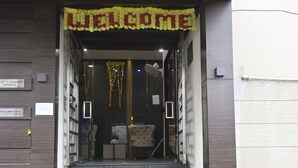 Entrada de un hotel con un letrero de 'WELCOME', una estatua de león y una escalera que conduce al interior.