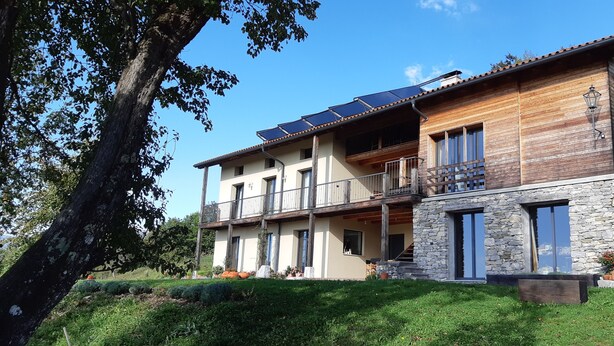 Une maison à deux étages dotée d’un balcon, de panneaux solaires et d’une façade en pierre.