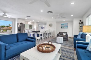 A modern living room with a blue sofa, a white coffee table, and a dining area with white chairs. - 5609 Del Rio Ct (Cape Coral)