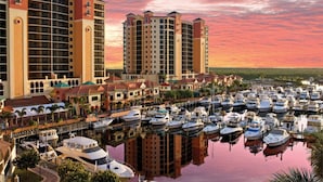 A marina with multiple boats docked, surrounded by high-rise buildings with balconies. - 5609 Del Rio Ct (Cape Coral)