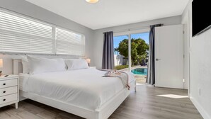 A modern bedroom with a large bed, a bedside table, and a view of a swimming pool. - 5609 Del Rio Ct (Cape Coral)