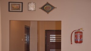 Un pasillo con un extintor de incendios montado en la pared, una puerta con un diseño a rayas y una obra de arte enmarcada sobre la puerta.