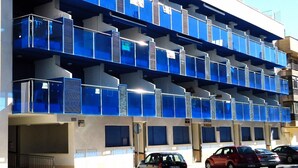 A multi-story building with blue balconies and a parking area with cars. - Maestro Roca Playavacaciones (Peñiscola)