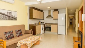 A compact living space with a kitchenette, a sofa with patterned cushions, a coffee table, and a television. - Maestro Roca Playavacaciones (Peñiscola)