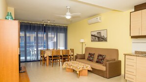 A living room with a sofa, coffee table, dining table, chairs, and a kitchen area with cabinets. - Maestro Roca Playavacaciones (Peñiscola)