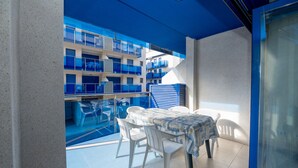 A balcony with a table and chairs, a view of a building with blue balconies, and a glass door. - Maestro Roca Playavacaciones (Peñiscola)