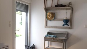 A bedroom with a bed, a small table, a hanging shelf with a hat and a fish ornament, and a bag on the floor.