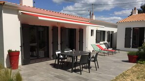 A patio area with a table and chairs, a covered seating area with lounge chairs, and a red and white awning.
