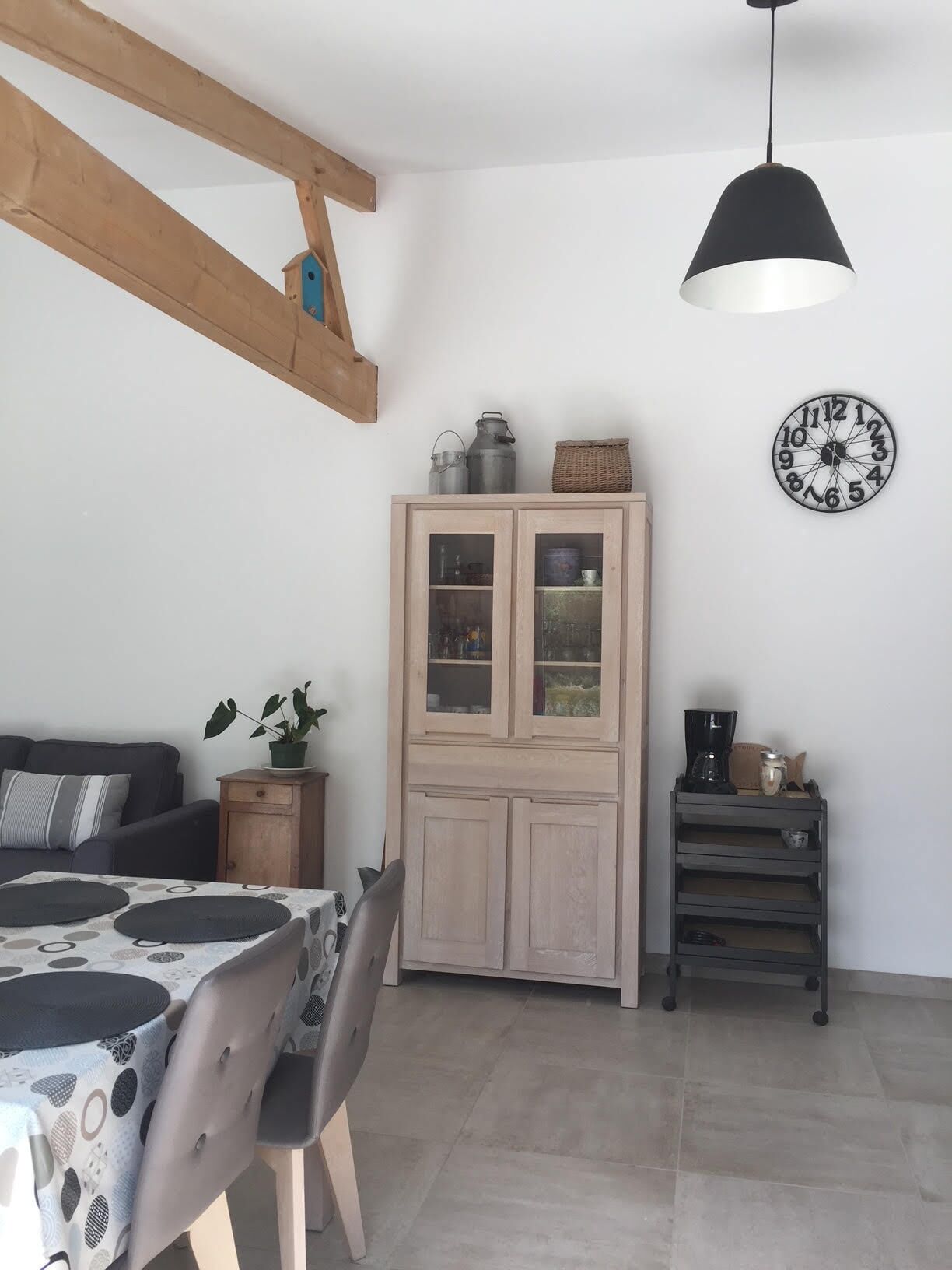 A room with a dining table, chairs, a cabinet, a clock, and a hanging light fixture.