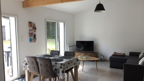 A modern living room with a dining area, a sofa set, a TV, and a large window.