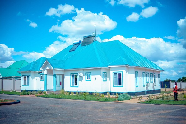 A single-story building with a blue roof and white walls, featuring a small garden in front. - Teranga Lodge & Restaurant (Mitumba)
