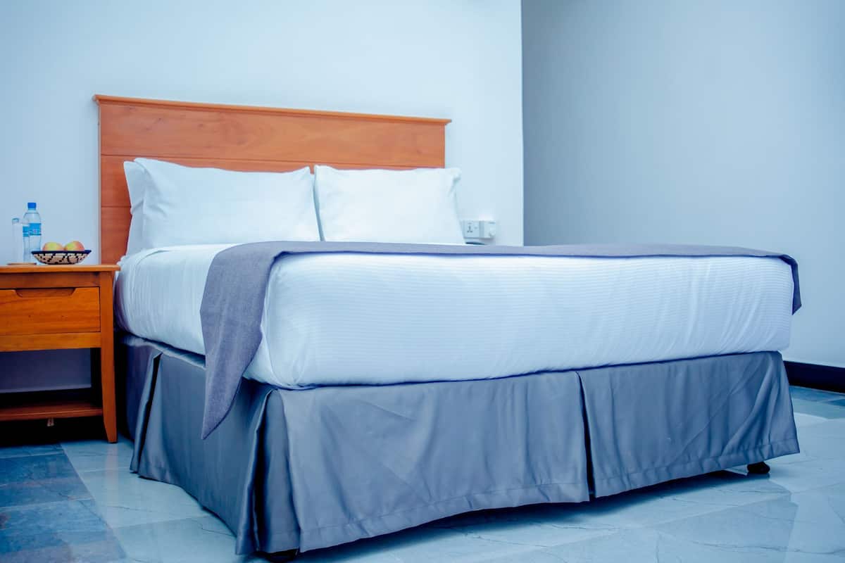 A neatly made bed with a wooden headboard, a grey skirt, and white pillows.