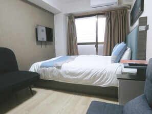 Une chambre d’hôtel avec un lit, une chaise, un bureau avec un clavier, un téléviseur fixé au mur et une fenêtre avec des rideaux.