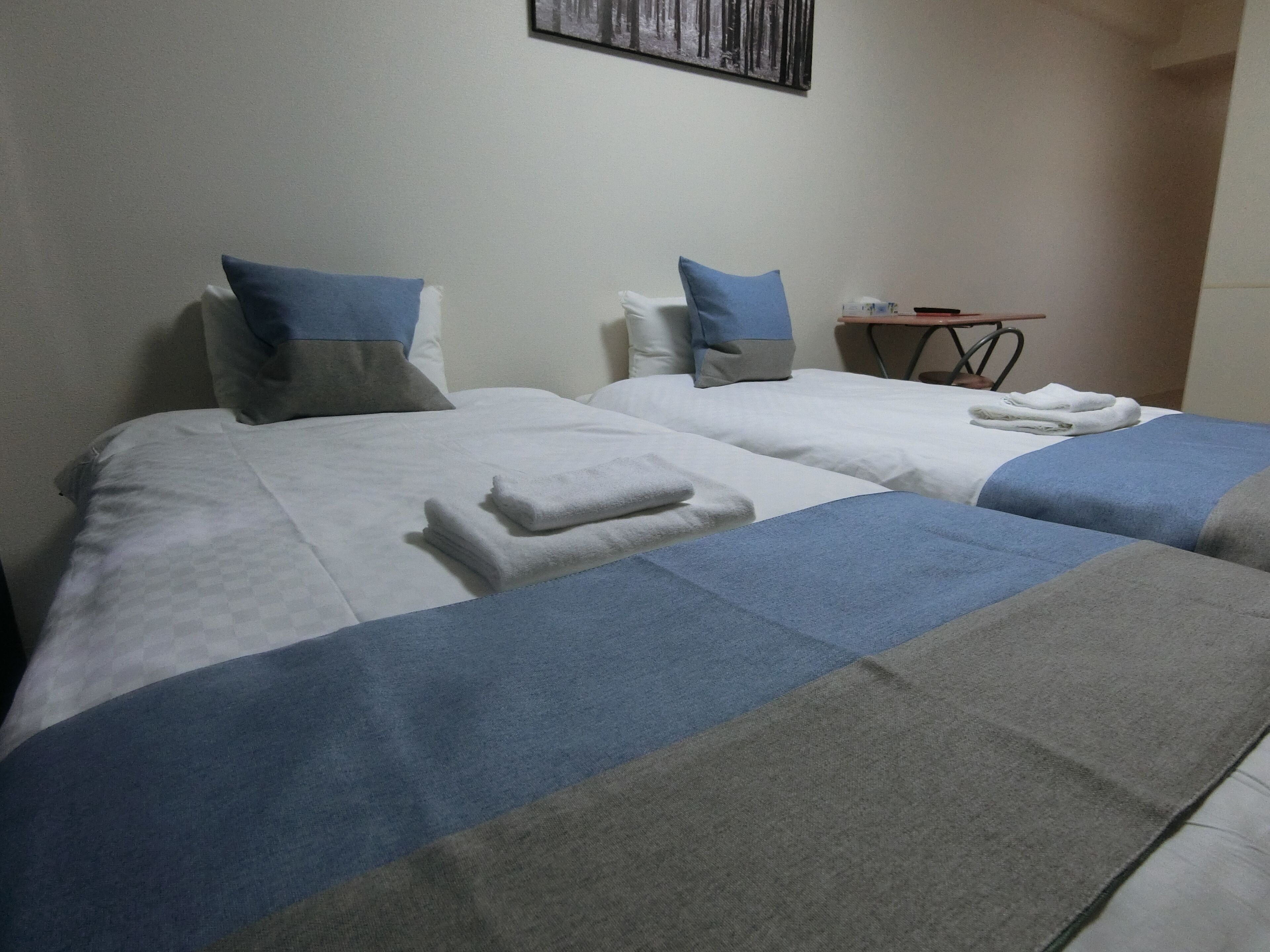 Une chambre d’hôtel avec deux lits, chacun recouvert d’une couverture bleue et grise, agrémentée d’oreillers blancs et de serviettes blanches pliées.