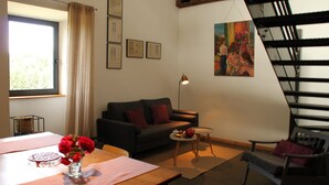 Una sala moderna con un sofá, una mesa de comedor con un florero, una mesita redonda con una lámpara y una escalera.