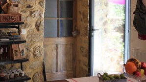 Un muro de piedra con un reloj, una puerta de madera, una mesa con sillas y una cesta de fruta.