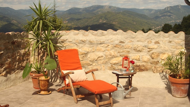 Un patio con una silla y mesa de madera, plantas en macetas y vistas a las montañas.