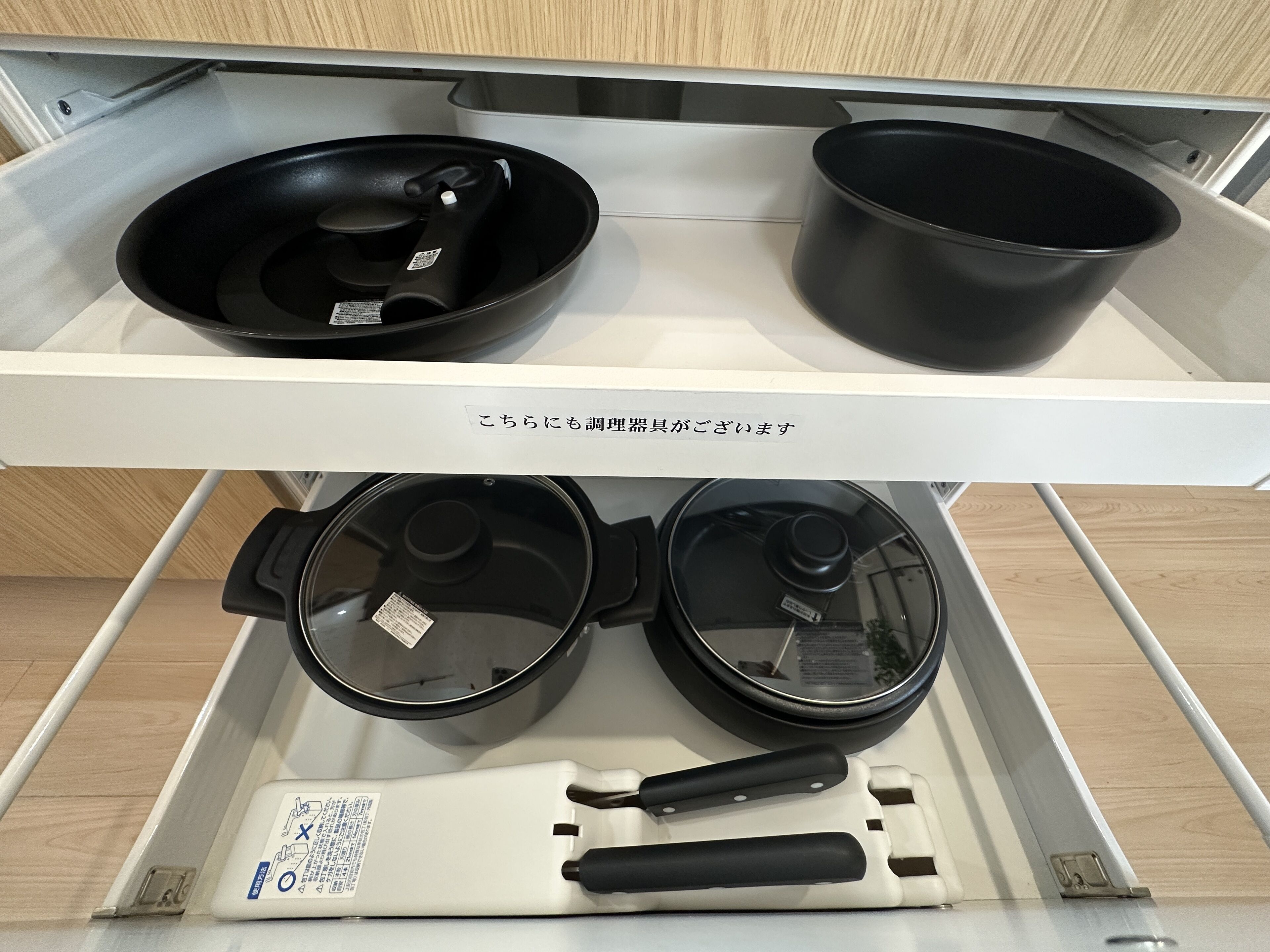 A kitchen drawer with two black frying pans and a white electric kettle.