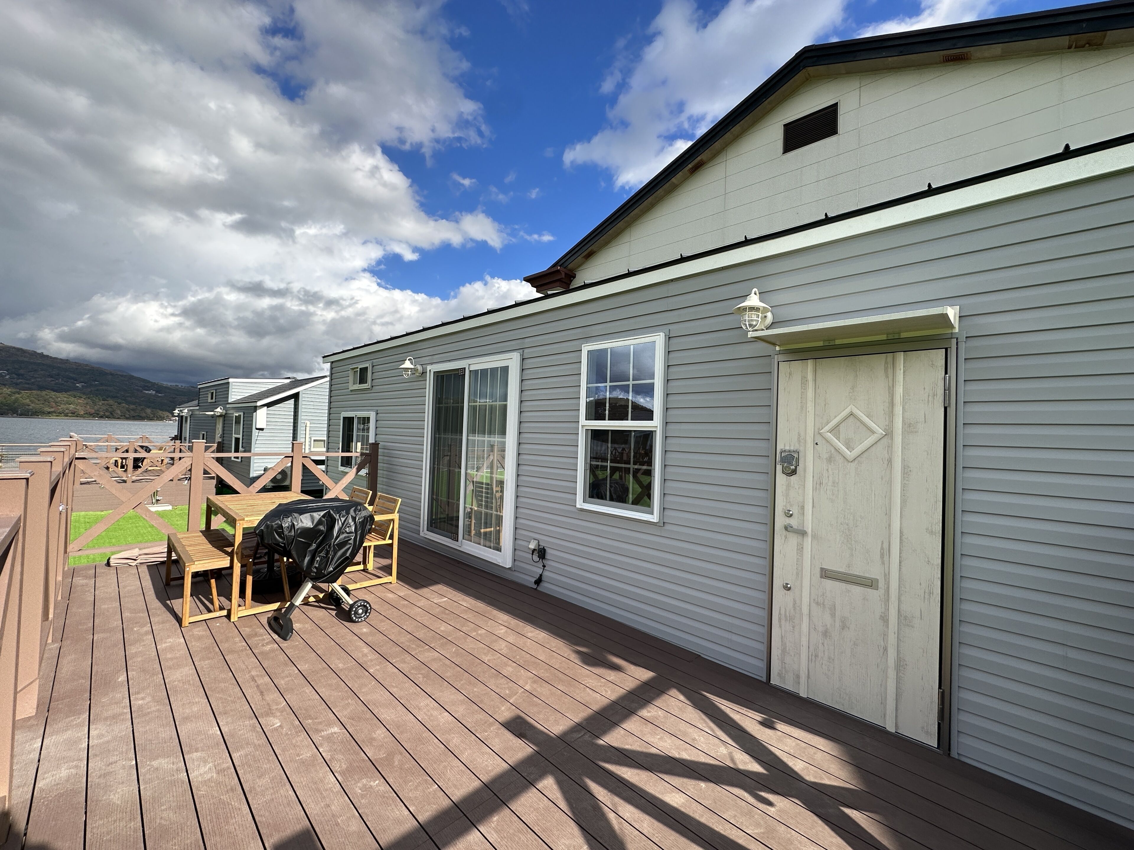 A deck with a covered seating area, a white door, and a view of a lake.