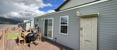 A deck with a covered seating area, a white door, and a view of a lake.