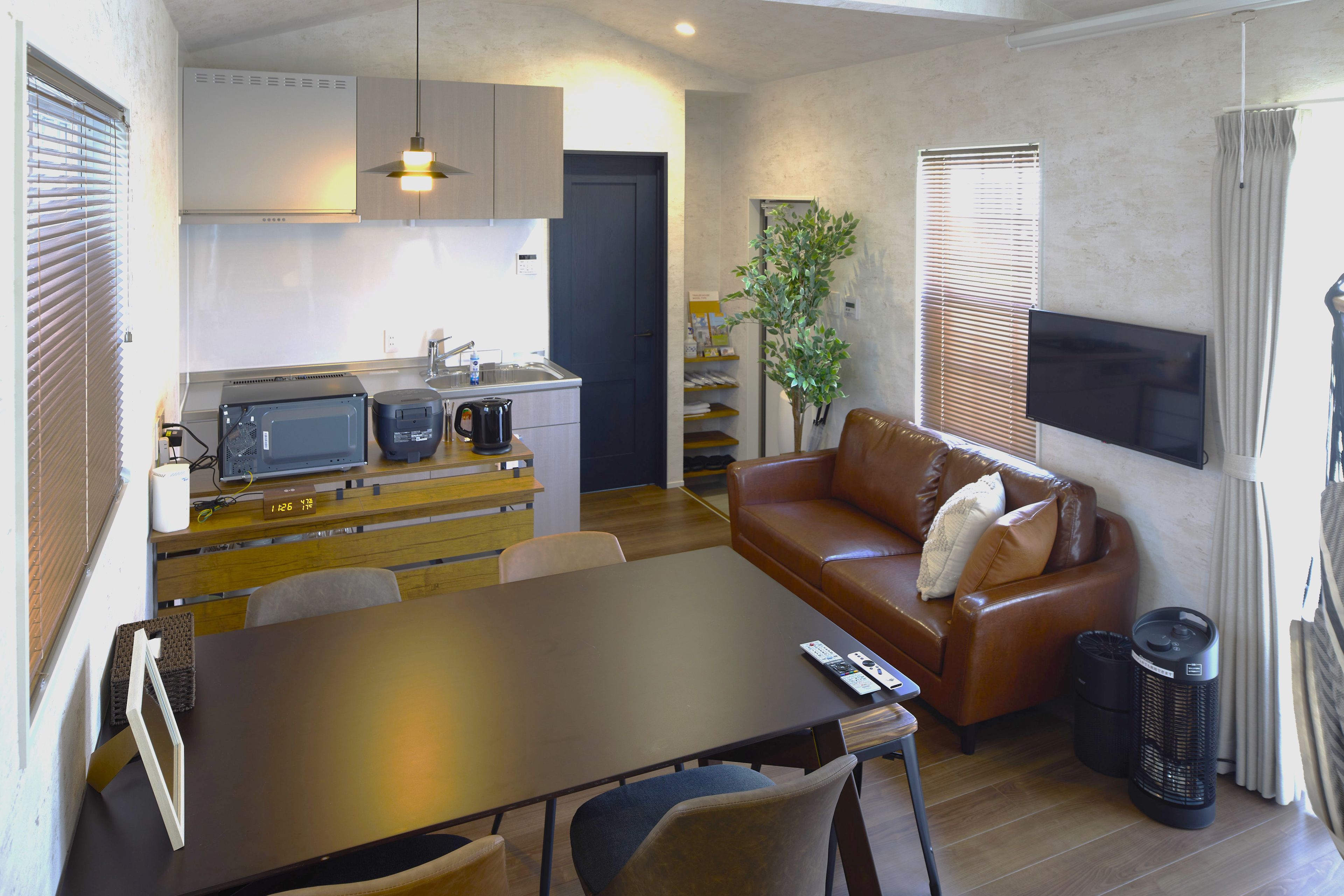 Espaço compacto para viver, com cozinha compacta, sofá, mesa de jantar e televisão fixada na parede.