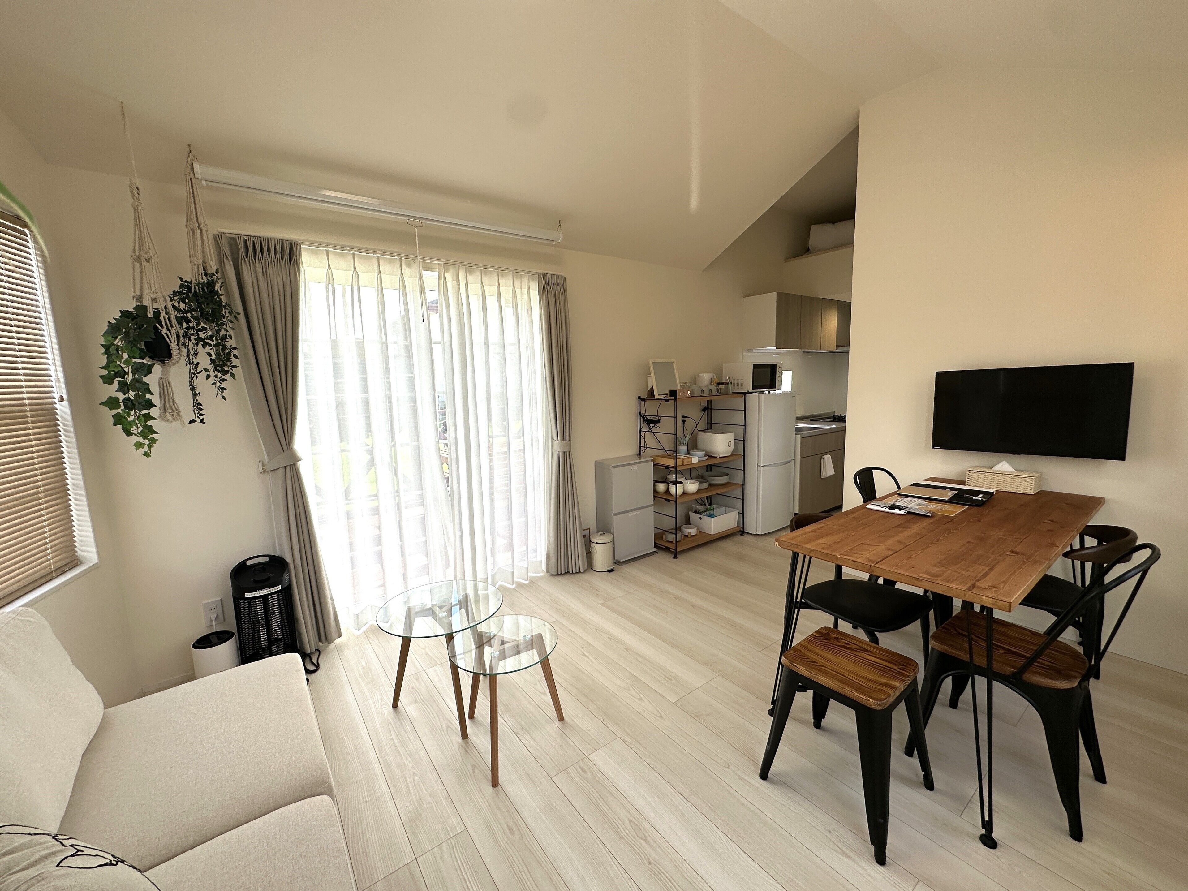 Een moderne woonkamer met een houten eettafel, een bank en een aan de muur bevestigde televisie.