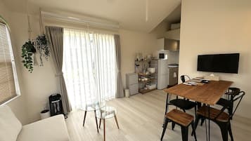 Een moderne woonkamer met een houten eettafel, een bank en een aan de muur bevestigde televisie.