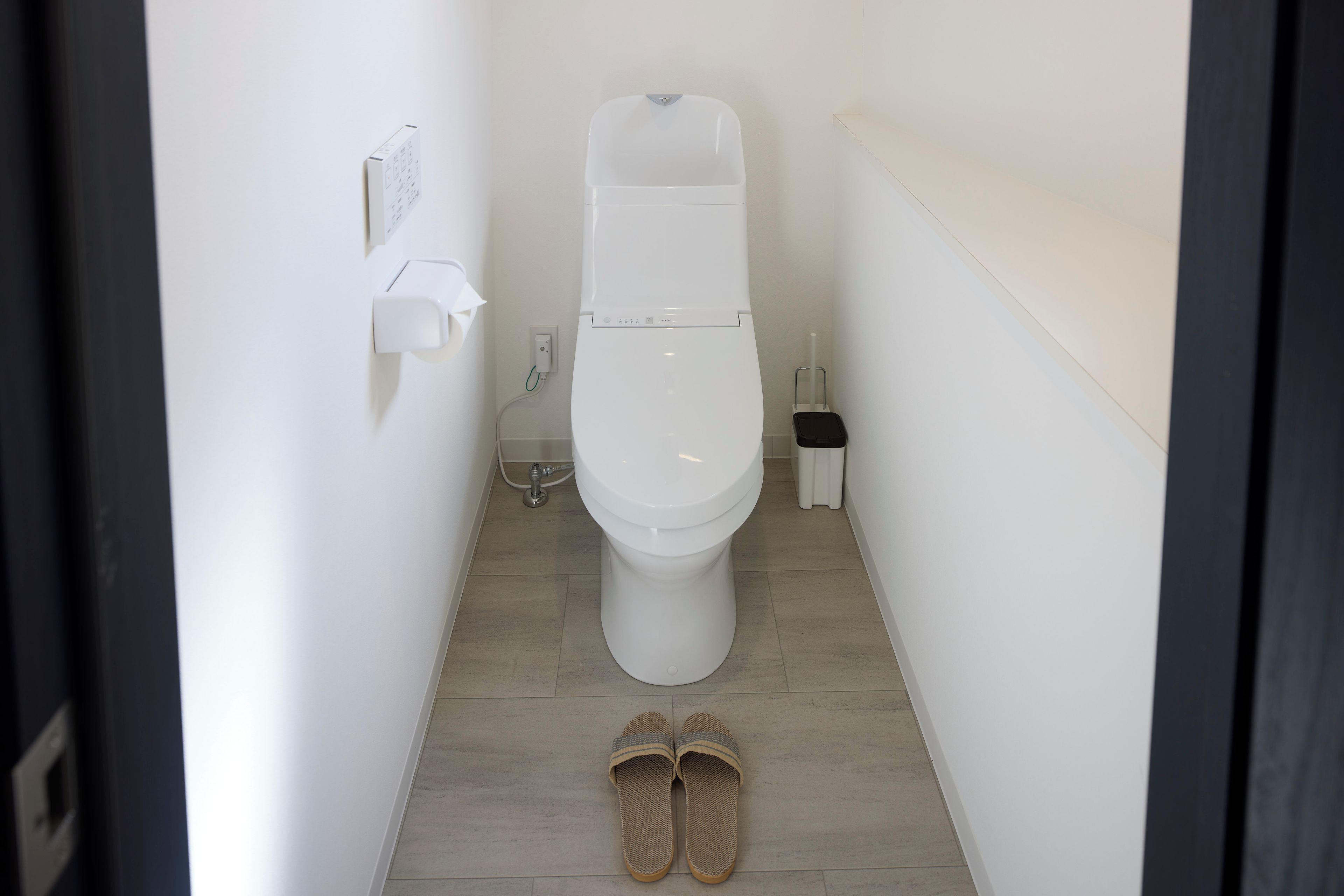 Un baño pequeño y estrecho con un inodoro, un secador de manos y un cubo de basura.