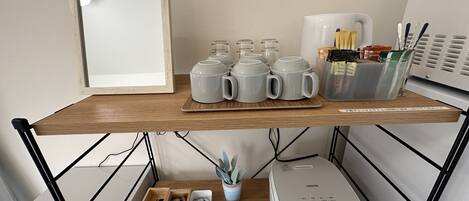 A kitchen counter with a coffee maker, mugs, and utensils.