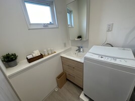 Un baño con un lavabo blanco, un espejo, una ventana, una planta pequeña y una lavadora blanca.