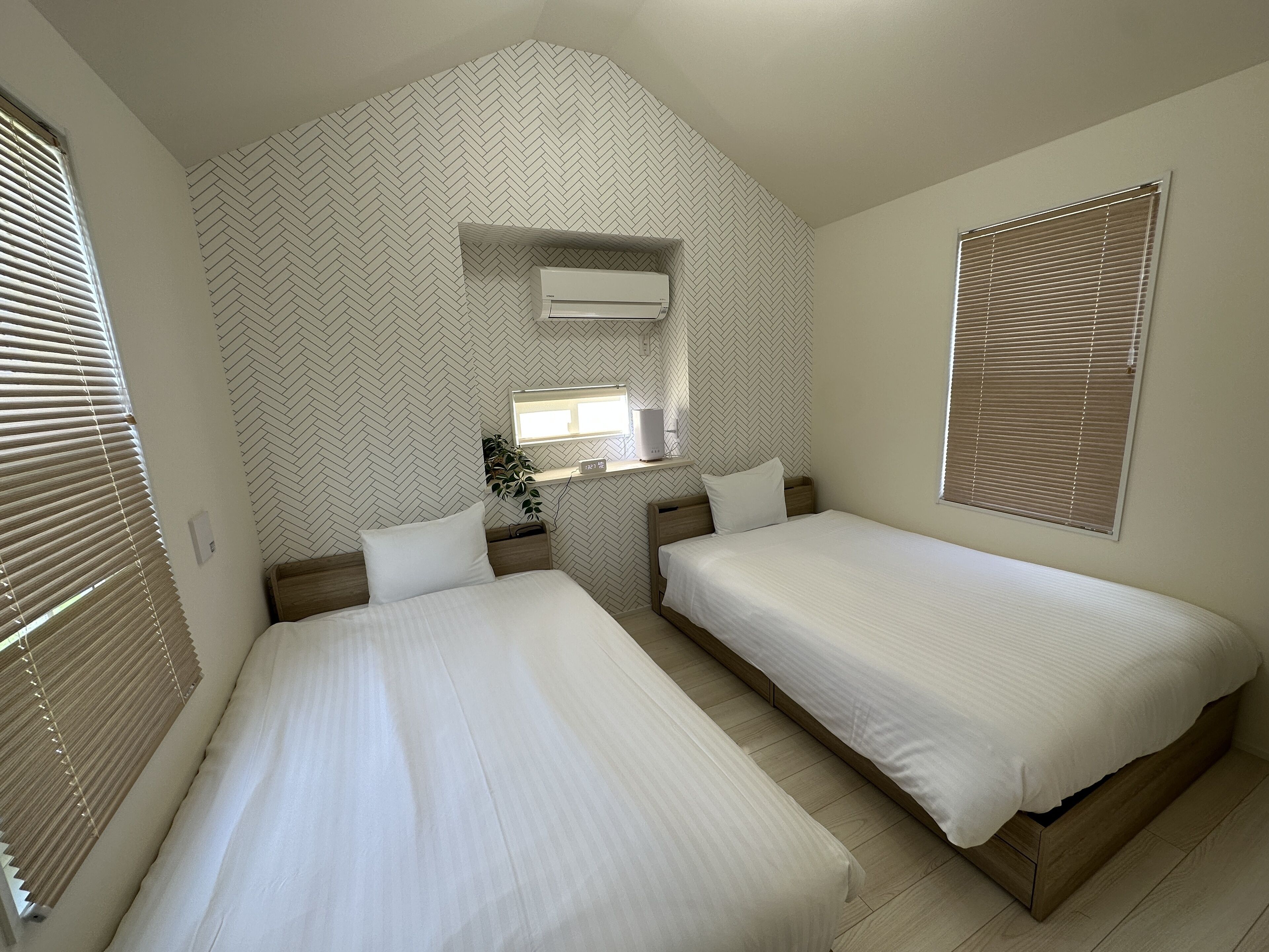 Une chambre avec deux lits, un miroir, une petite fenêtre et un climatiseur fixé au mur.