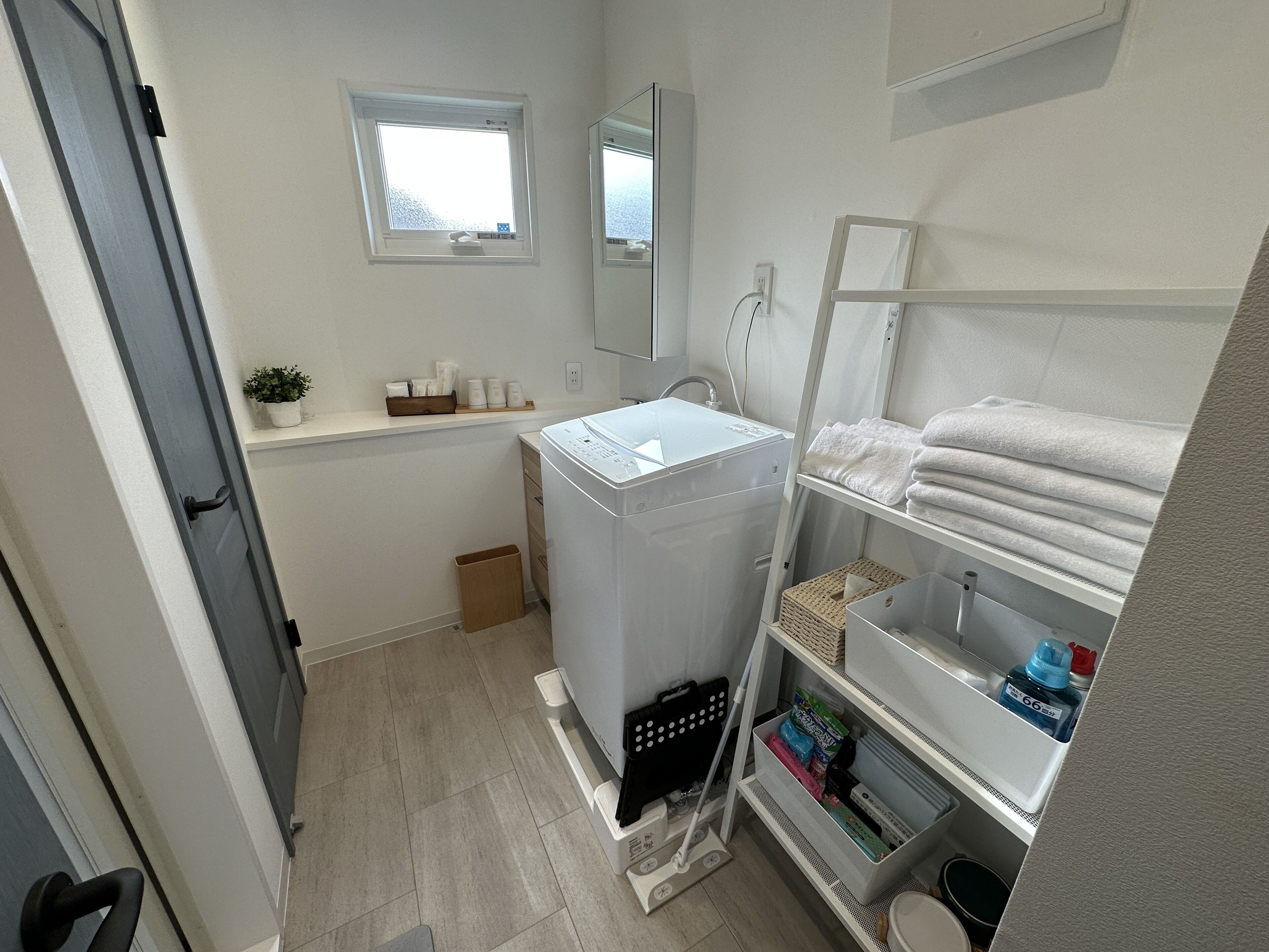 Un baño pequeño con lavadora, un estante con toallas, una ventana y un espejo.