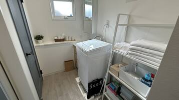 Un baño pequeño con lavadora, un estante con toallas, una ventana y un espejo.