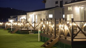 A row of cabins with wooden decks and string lights, set against a backdrop of a hill and a building. - SolanaFujiyamanakako (Yamanakako)