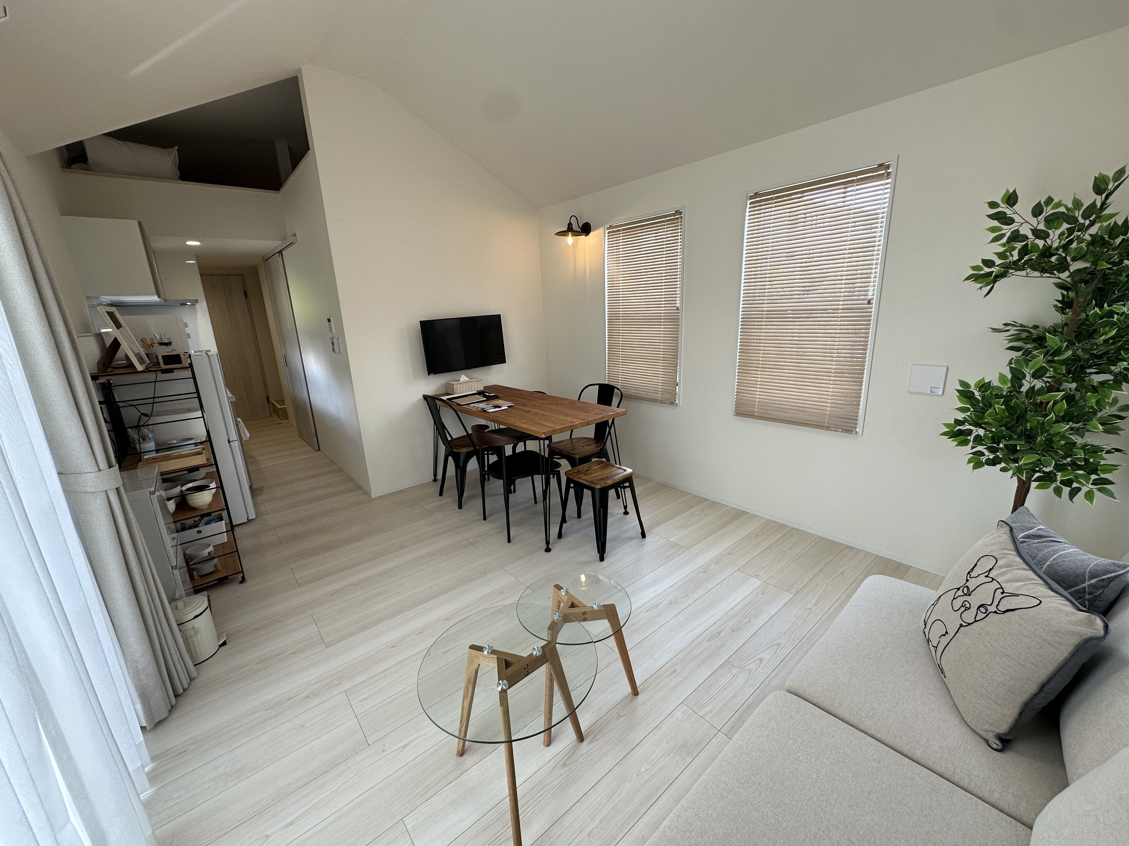 Un salon moderne avec une table à manger en bois, une table basse en verre et un canapé agrémenté d’un coussin décoratif.