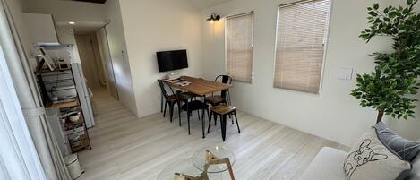 Un salon moderne avec une table à manger en bois, une table basse en verre et un canapé agrémenté d’un coussin décoratif.