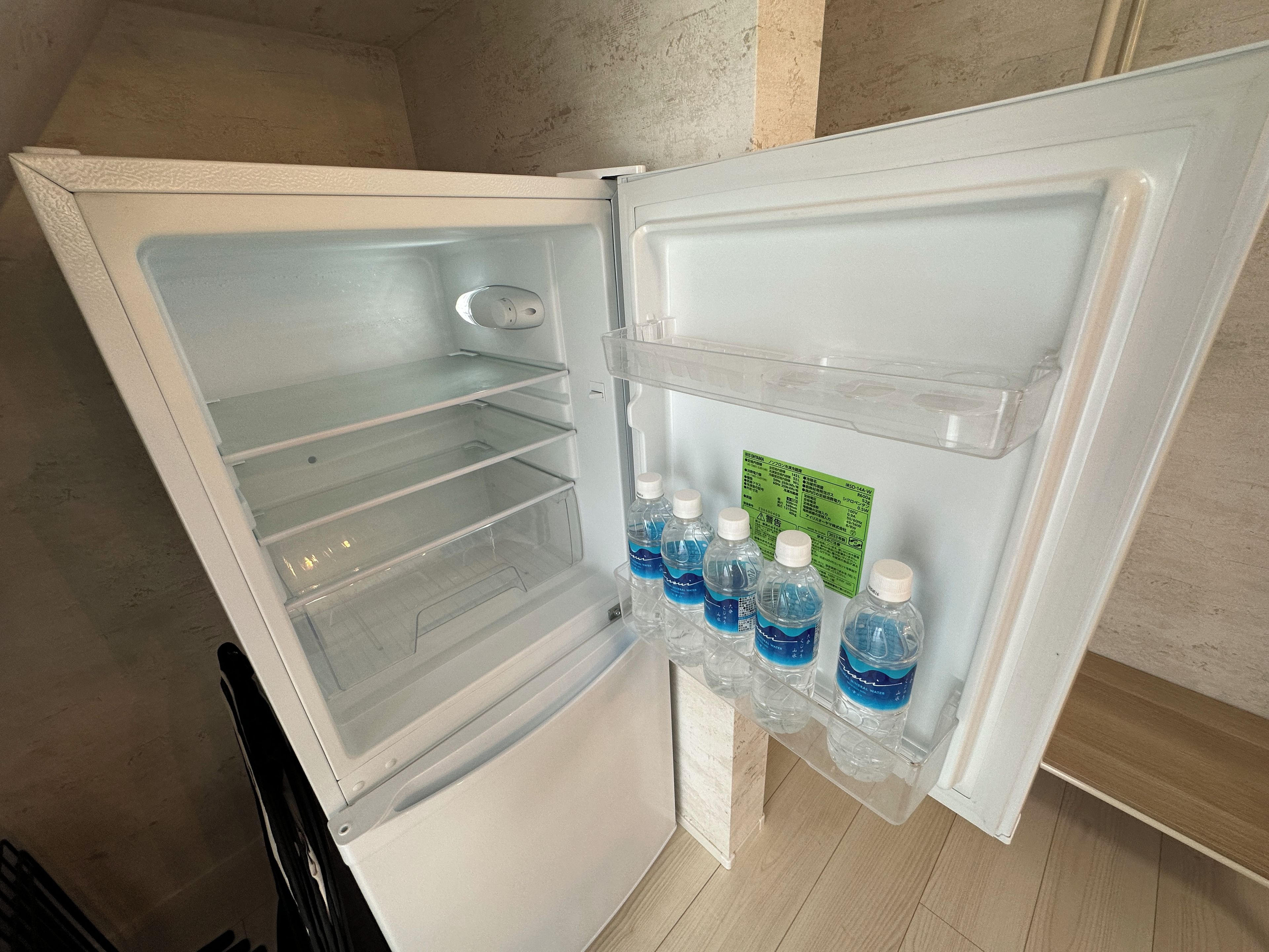 An open refrigerator with clear shelves and a water dispenser.