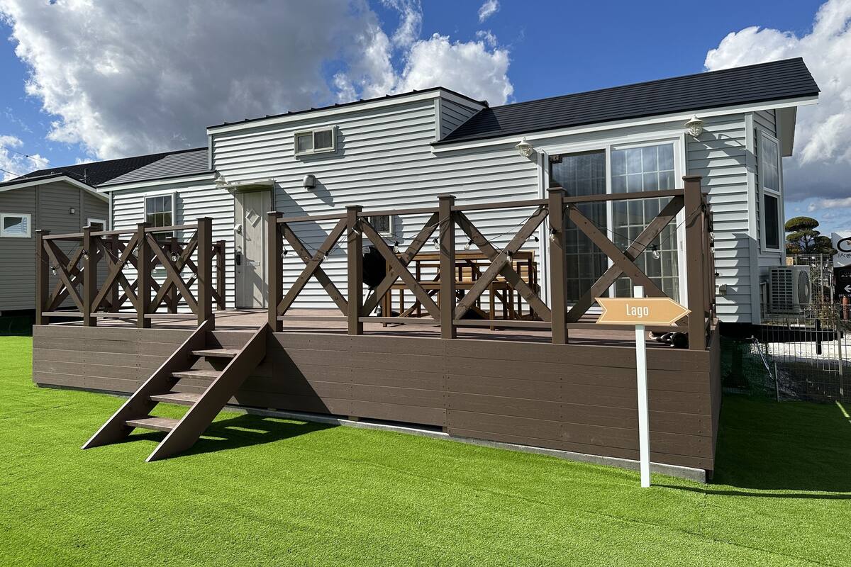 Una casa móvil blanca con una terraza de madera, una rampa y un letrero que indica 'Lago'.